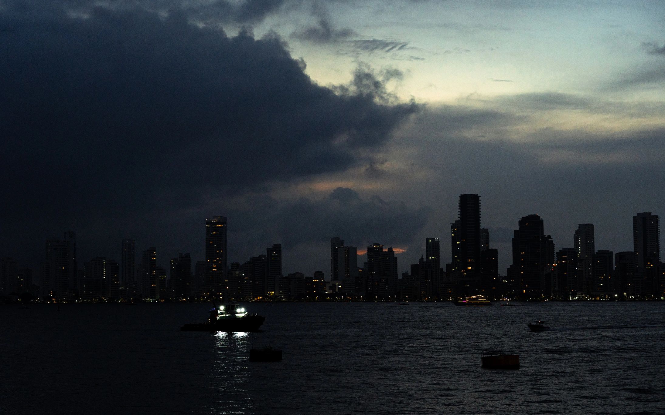 City skyline silhouettes against dark evening sky with boats